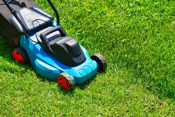 Cortacésped en un césped verde exuberante, la mitad de la hierba recortada. Patio trasero de la casa. — Foto de Stock