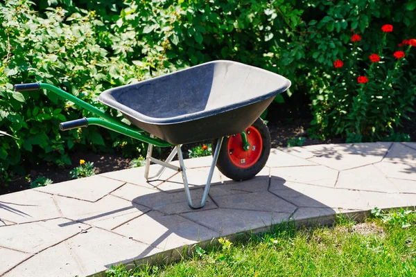 Chariot de jardin en plastique et métal neuf dans un jardin botanique. Travaux de jardin, dans la partie du jardin fleuri — Photo
