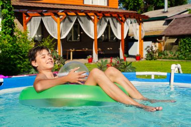 Yeşil çemberli bir yaz havuzu ve gülen bir adam. Doymuş mavi su arka planı. Yaz tatili, kahkaha, hayatın neşesi ve neşeli bir adam.