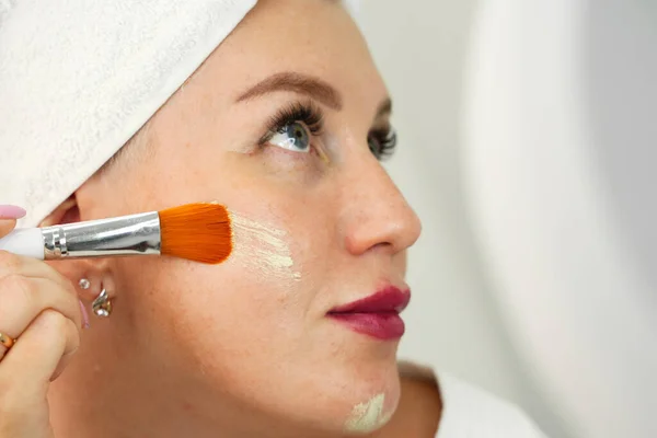 Woman applies makeup to her face, selective focus on skin and brush. Applying foundation to pigmented skin with a brush. Overlapping skin imperfections with cosmetics.