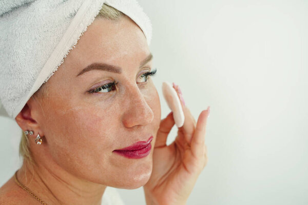 Young woman in bath towel on head apply cleansing tonic with cotton pads. Girl remove makeup with micellar water. Face cleanser. Pure healthy skin. Morning facial treat. Mirror reflection at bathroom