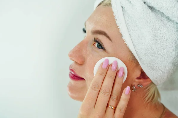 Una donna si toglie il trucco con un tovagliolo in bagno, si pulisce il viso con un batuffolo di cotone. Detergente e idratante per l'invecchiamento della pelle, la cura e l'idratazione — Foto Stock