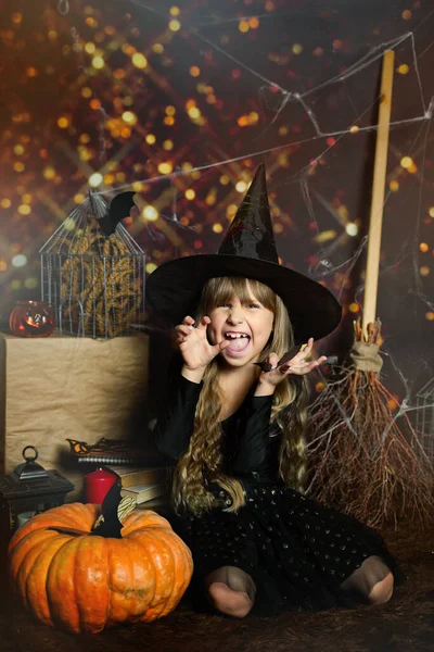 Copy space for Happy Halloween on the photo Preschool girl scares, expression of emotions evil laughter in a witchs hat with a pumpkin