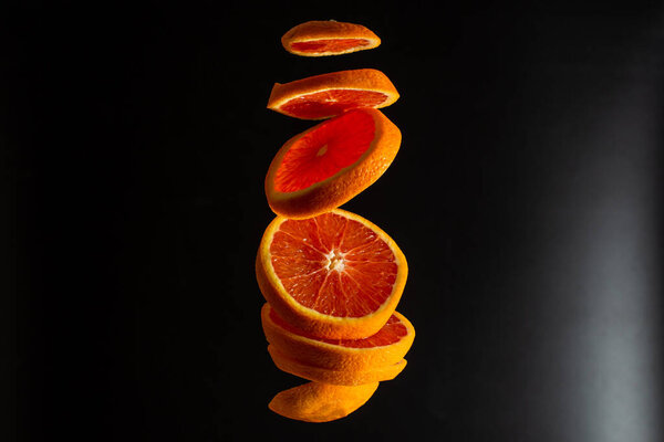 A sliced red orange levitates in the air. Creative photo of flying orange on black background