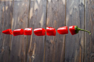 Doğranmış kırmızı biber havada uçar gider. Karanlık bir ahşap arka planda uçan biberin yaratıcı fotoğrafı.