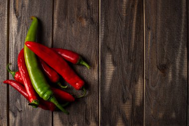Taze kırmızı ve yeşil biberler eskimiş bir ahşabın arka planına eşit olarak yayılmış..