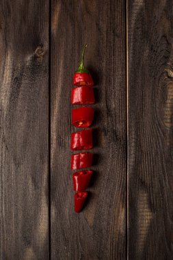 Taze kırmızı biber, parçalara ayrılmış, eski siyah ahşaptan yapılmış bir masanın üzerine uzanmış. Ahşap arkaplan.