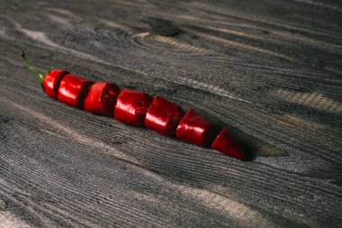 Taze kırmızı biber, parçalara ayrılmış, eski siyah ahşaptan yapılmış bir masanın üzerine uzanmış. Ahşap arkaplan.