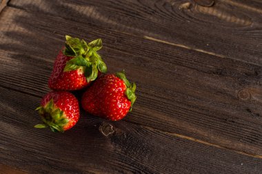 Üç taze sulu çilek, eski bir masada, koyu bir ahşap arka planda yatıyor..