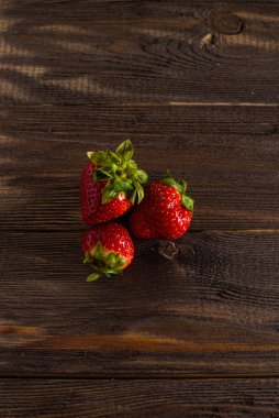 Üç taze sulu çilek, eski bir masada, koyu bir ahşap arka planda yatıyor..
