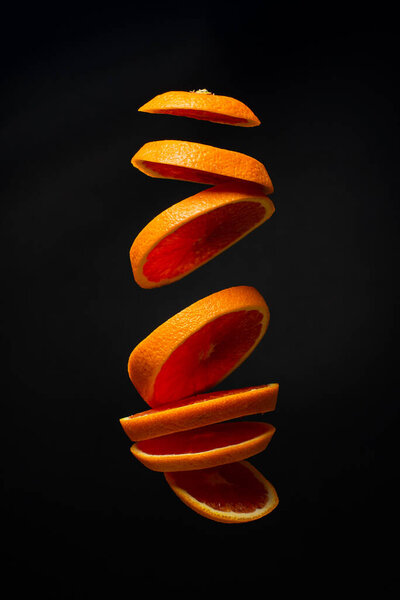 A sliced red orange levitates in the air. Creative photo of flying orange on black background