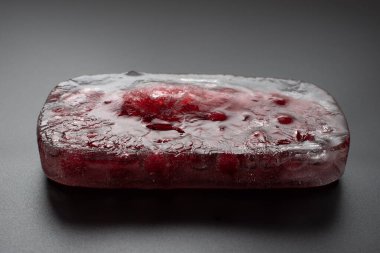 Frenk üzümü, siyah arka planda bir parça buzun içinde donmuş. Yakın plan.