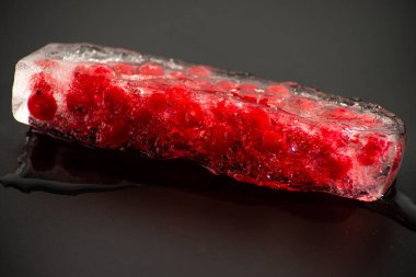 Frenk üzümü, siyah arka planda bir parça buzun içinde donmuş. Yakın plan.