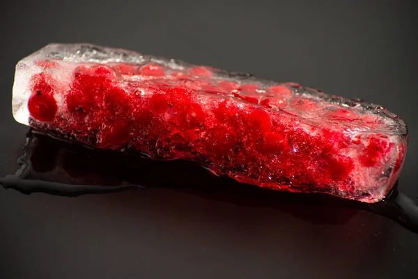 Frenk üzümü, siyah arka planda bir parça buzun içinde donmuş. Yakın plan.