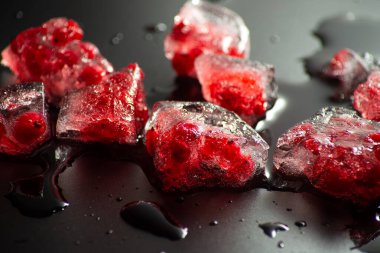 Kırık bir buzun içinde donmuş kırmızı frenk üzümü ve siyah bir arka plan. Eriyen buz briketine yakın plan