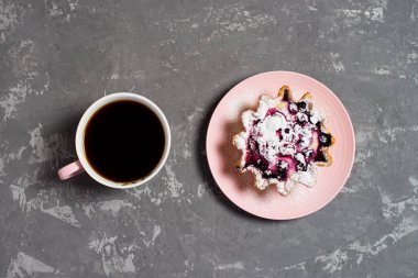 Fincanda taze sade kahve. Süzme peynir ve böğürtlenli kek sepeti, üzerine pudra şekeri serpilmiş. Beton bir masanın arka planında kahvaltı. Düz.