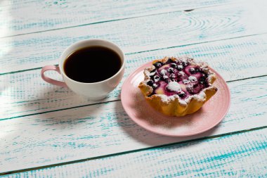 Bir fincan kahve ve üzerinde böğürtlen ve süzme peynir olan bir kek sepeti klasik beyaz ve mavi bir masa. Sabah kahvaltısı.