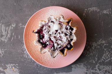 Pembe bir fincan tabağında çilek ve süzme peynirli kek sepeti. Taze çilek ve süzme peynirli büyük tart, üzerine pudra şekeri serpiştirilmiş. Düz beton arkaplan