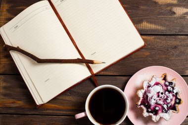 Düztaban çizimi. Açık defter, eski bir dal kalem, fincanda sade kahve ve eski bir ahşap masanın üstünde böğürtlenli kek sepeti..