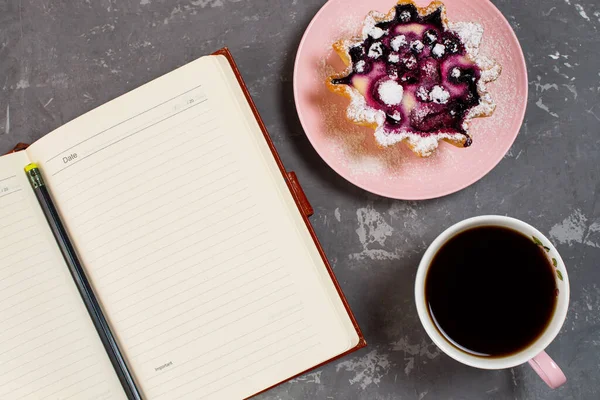 Notepad, a cup of coffee and a cake basket with berries and cottage cheese on a concrete table. Flatley coffee break layout.