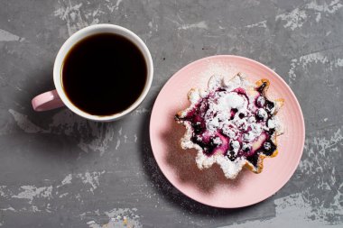 Fincanda taze sade kahve. Süzme peynir ve böğürtlenli kek sepeti, üzerine pudra şekeri serpilmiş. Beton bir masanın arka planında kahvaltı. Düz.