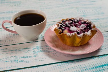Bir fincan kahve ve üzerinde böğürtlen ve süzme peynir olan bir kek sepeti klasik beyaz ve mavi bir masa. Sabah kahvaltısı.