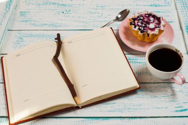 Not defteri, bir fincan kahve ve içinde böğürtlen ve süzme peynir olan klasik mavi beyaz renkli bir kek sepeti. Sabah kahvaltısı.