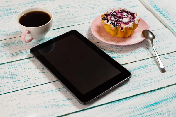 A digital tablet, a cup of coffee and a cake basket with berries and cottage cheese on a white and blue vintage table. Morning breakfast background.