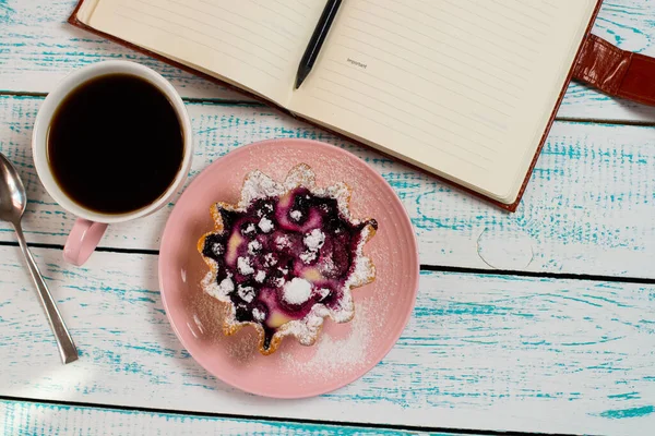 Notepad, a cup of coffee and a cake basket with berries and cottage cheese on a vintage blue and white color. Morning breakfast background. Flatley coffee break layout.