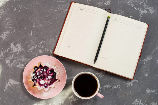 Notepad, a cup of coffee and a cake basket with berries and cottage cheese on a concrete table. Flatley coffee break layout.