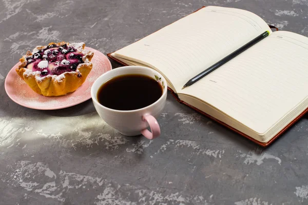 Notepad, a cup of coffee and a cake basket with berries and cottage cheese on a concrete table. Flatley coffee break layout.