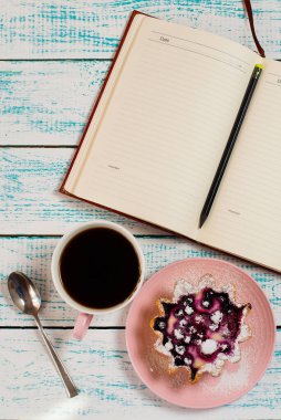 Not defteri, bir fincan kahve ve içinde böğürtlen ve süzme peynir olan klasik mavi beyaz renkli bir kek sepeti. Sabah kahvaltısı. Düz kahve molası düzeni.