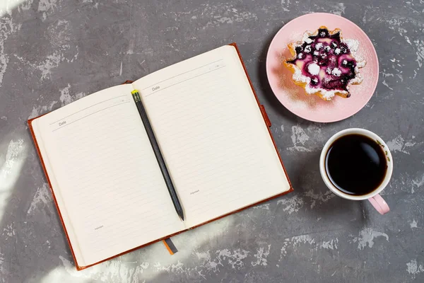 Notepad, a cup of coffee and a cake basket with berries and cottage cheese on a concrete table. Flatley coffee break layout.