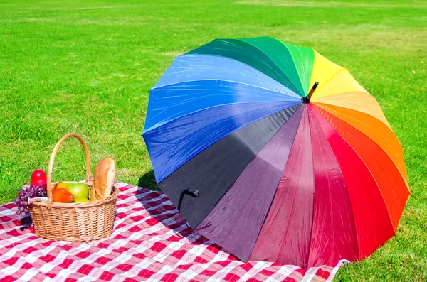 Guarda-chuva arco-íris e cesta de piquenique — Fotografia de Stock