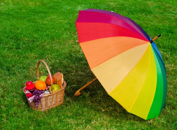 Guarda-chuva arco-íris e cesta de piquenique — Fotografia de Stock