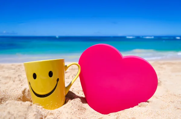 Happy face mug with heart shape on the beach — Stock Photo, Image
