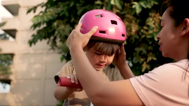 在暑期公园学习骑摩托车之前 年轻的母亲帮助女儿戴着粉色的头盔 积极为儿童提供户外运动 — 图库视频影像