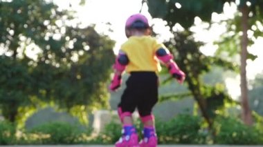 Koruyucu pedler takan ve kasklı küçük bir kız yaz parkında paten kaymayı öğreniyor. Çocuklar için aktif açık hava sporu.