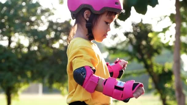 夏の公園でローラースケートに保護パッドと安全ヘルメットの学習を身に着けている女の子 子供のためのアクティブな屋外スポーツ — ストック動画