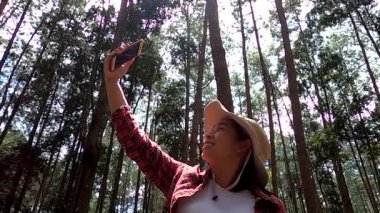 Mutlu kadın yürüyüşçüler, ağaçların arka planında ulusal parkta internetten akıllı telefon görüntülerini kullanıyorlar. Seyahat ve tatil kavramı.