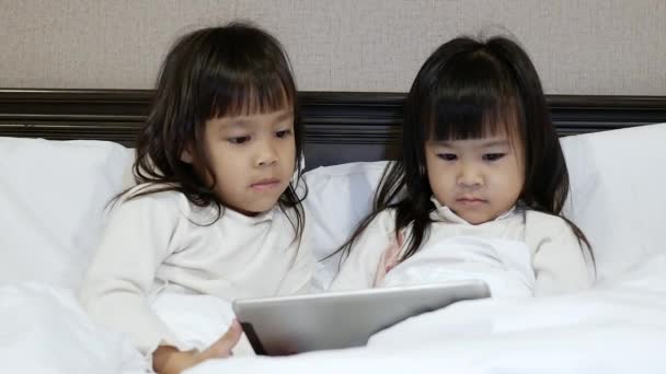 幸せな兄弟女の子見ながらデジタルタブレットパッド一緒にベッドの上に家に横たわって — ストック動画