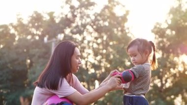 Genç anne, yaz parkında scooter sürmeyi öğrendikten sonra kızının dirsek koruyucusunu kaldırmasına yardım ediyor. Çocuklar için aktif açık hava sporu.