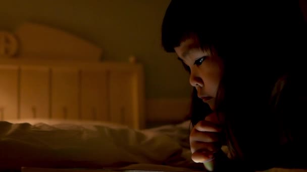 かわいい女の子は夜にデジタルタブレットでビデオを見て 顔に反射した光は 視覚障害を引き起こし 子供たちが過活動を引き起こす効果を持つことができます — ストック動画