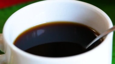 El 'in şekeri kaşıkla aromalı kahveye karıştırdığı yakın plan. Bir fincan aromatik kahve ahşap bir masaya konur..