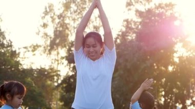 Aile yoga yapıyor. İki küçük kız ve anne açık havada bir yaz parkında dengede duruyorlar. Tatilde aile sağlık hizmetleri.