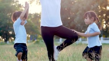 Aile yoga yapıyor. İki küçük kız ve anne açık havada bir yaz parkında dengede duruyorlar. Tatilde aile sağlık hizmetleri.