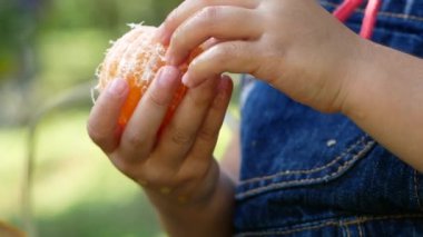 Portakal soyan, portakal soyan ve mutlulukla yemek yiyen tatlı küçük kız. Sağlıklı yemek..