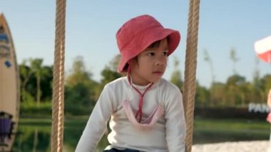 Güneşli bir günde gölün kenarında sallanan tatlı küçük kız beyaz kumsalın arka planında..