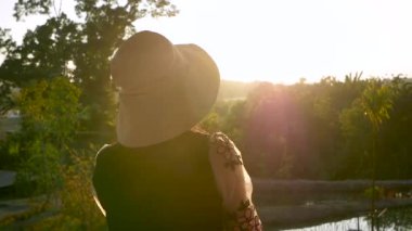 Doğayla eğlenen genç bir kadın ve bahçedeki günbatımının arka planına bakan bir gülümseme..