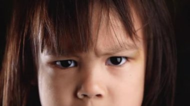 Evdeki karanlık odada, gözlerinde pişmanlık ve hoşnutsuzlukla kameraya bakan kızgın küçük bir kızın yakın plan portresi. Mutsuz bir çocukluk konsepti.